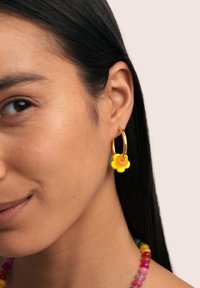 Boucles d'oreilles en forme de fleur jaunes avec un anneau en or, présentant un design multicolore et une texture lisse, exposées aux côtés d'un collier en perles.