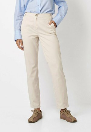 Beige Baumwollhosen im Slim-Fit-Design, mit vorderen Taschen und Knopfverschluss, kombiniert mit braunen sportlichen Sneakers.