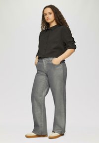 Grijze denim wijde broek met een hoge taille, gecombineerd met een zwart button-up shirt. Schoenen zijn crème met een lichtbruine zool.