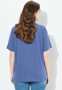 Niebieska koszulka z krótkim rękawem o nieco luźniejszym kroju, wykonana z miękkiego materiału, z okrągłym dekoltem i bez widocznych wzorów czy nadruków.