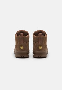 Hnědé semišové kotníkové boty se strukturální povrchovou úpravou. Obsahují hnědou gumovou podrážku, zadní poutko a zlaté logo na podpatku.