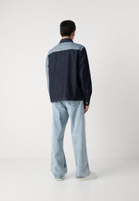 Denimjakke med mørkeblå kropp og lys blå yoke, strukturert passform, lange ermer og knappelommer, sammen med lysvaskede vidbukser.