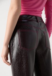 Kalhoty s vysokým pasem v tmavě burgundy barvě z umělé kůže s lesklým povrchem, zvýrazněné kontrastním růžovým prošíváním a dvěma zadními kapsami.