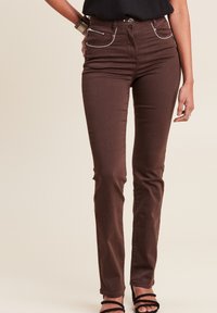 Braune Jeanshose mit schlanker Passform, ausgestattet mit zwei vorderen Taschen mit silbernen Reißverschlüssen, weißen Nähakzenten und einem Knopfverschluss.