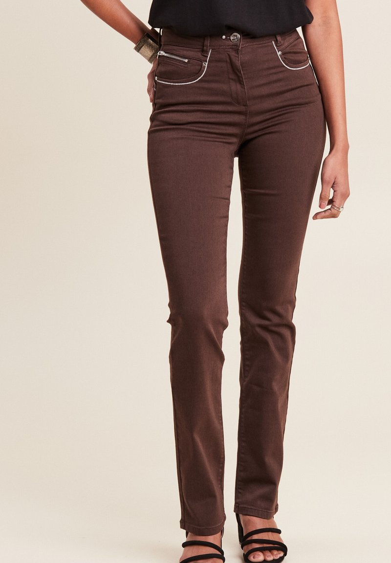 Braune Jeanshose mit schlanker Passform, ausgestattet mit zwei vorderen Taschen mit silbernen Reißverschlüssen, weißen Nähakzenten und einem Knopfverschluss.