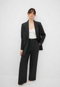 Mörk randig kostym med en skräddarsydd blazer och vida byxor, parat med en vit camisole och ljusa högklackade skor.