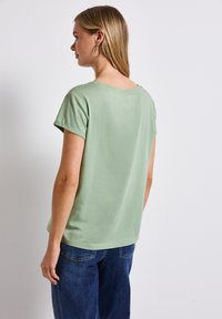 Krátký rukáv, světle zelené tričko vyrobené z měkké tkaniny, s kulatým výstřihem a volným střihem, doplněné tmavě modrými džíny.