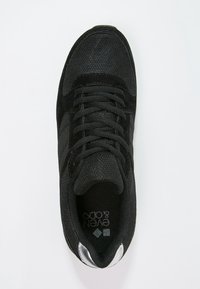 Chaussure de sport noire avec un dessus en tissu en maille et en suede, design à lacets, languette rembourrée, accents réfléchissants et semelle texturée.
