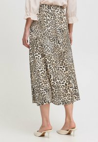 Jupe midi imprimée léopard en beige et noir, fabriquée en tissu lisse. Présente une silhouette évasée avec un détail de couture à l'arrière.