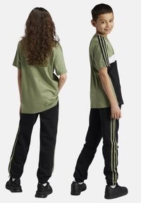 Camiseta de algodón verde con detalles en blanco y negro, combinada con pantalones de chándal negros con franjas laterales verdes. Ropa casual para niños.
