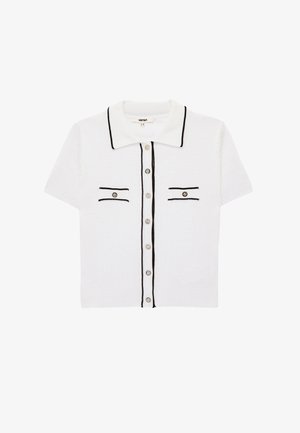 Witte polo met korte mouwen met zwarte afwerking, twee kleine voorzakjes met zwarte rand en zilveren knopen op de voorkant.
