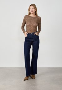 Top a maniche lunghe, aderente, di colore marrone con motivo a stampa leopardata, abbinato a jeans ampi blu scuro e décolleté marroni a punta.
