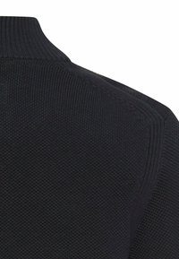 Czarny dziergany sweter z fakturowanej tkaniny. Posiada wysoki kołnierz oraz subtelne prążkowane detale przy szyi i ramionach.