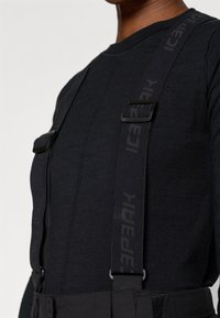 Pulover negru din tricot cu mânecă lungă, dintr-un material texturat, având bretele negre ajustabile cu un logo. Design minimalist axat pe funcționalitate.