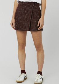 Jupe en tweed bordeaux avec un motif texturé, un design portefeuille et une fermeture à bouton. Associée à des baskets blanches et des chaussettes bordeaux.