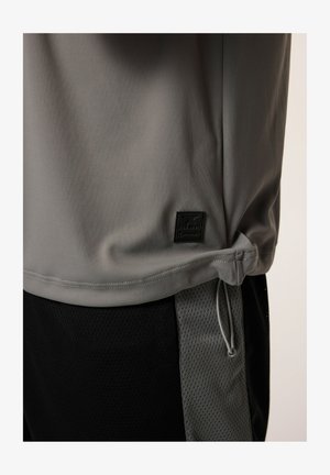 Maglietta atletica grigia con tessuto liscio, dotata di una toppa logo nera, cordino laterale e abbinata a pantaloni corti in rete neri.