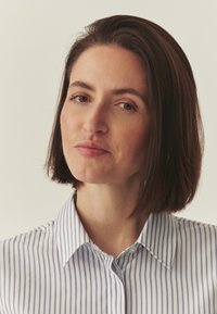 Une personne aux cheveux courts, brun foncé, porte une chemise à col avec des rayures verticales bleues et blanches, dotée d'une patte de boutonnage et d'une texture lisse.