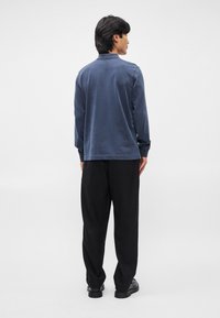 Σακάκι ναυτικό μπλε με μακριά μανίκια και γιακά, μαλακή υφή και διακριτές ραφές, σε συνδυασμό με χαλαρούς μαύρους παν trousers και μαύρα παπούτσια.