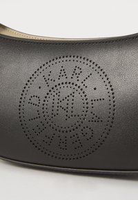 Svart lærko med perforert design og sirkulært logo. Glatt tekstur, rund form og kontrastfarge på innersålen synlig.