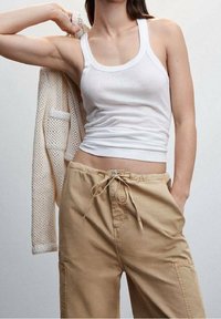 Un débardeur blanc à côtes associé à un pantalon cargo beige avec cordons de serrage. Un cardigan en maille crème repose sur une épaule.