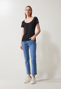 Svart kortermet t-skjorte med rund hals, kombinert med lyseblå rette jeans og hvite joggesko. Enkel design med et rent og uformelt utseende.