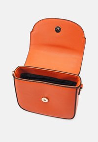 Pomarańczowa skórzana torba na ramię z czarną lamówką. Posiada zatrzask oraz otwarte wnętrze. Gładka faktura, kompaktowy, prostokątny kształt.