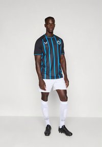 Černý fotbalový dres s tyrkysovými pruhy a logem. Kombinován s bílými šortkami a bílými podkolenkami s motivem po kolena. Černé kopačky.