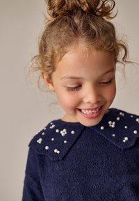 Marineblau gestrickter Pullover mit einem strukturierten Muster, ausgestattet mit einem großen Kragen, der über die Brust mit perlenartigen Verzierungen geschmückt ist.