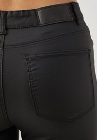 Jeans in denim nero con una texture liscia, design a cinque tasche e un piccolo etichetta in vita. Cuciture pulite e forma aderente.