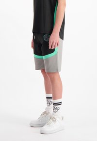 Zwarte en grijze sportshorts met een groene accent langs de zoom en een geometrisch logo. Gecombineerd met witte sneakers en gestreepte sokken.
