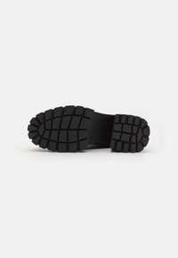Semelle de chaussure en caoutchouc noir avec un motif de semelle profond et symétrique, aux bords arrondis pour une meilleure adhérence. Le matériau semble mat et durable.