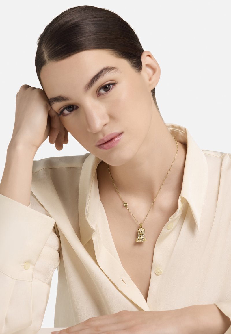 Arany nyaklánc részletes medállal, amely egy medve formáját ábrázolja, finom lánccal és a kapocs közelében egy kis kerek díszítéssel.