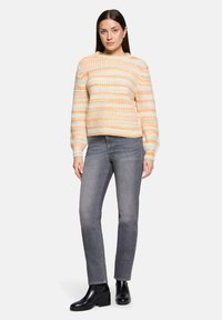 Sweter z dzianiny z pastelowymi poziomymi paskami w kolorze pomarańczowym, żółtym i kremowym. Połączony z szarymi dżinsami i czarnymi botkami do kostki. Projekt z długim rękawem.