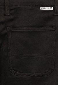 Crni denimski materijal s stražnjim džepom koji ima ravno šivanje. Oznaka "JACK & JONES" nalazi se iznad džepa.