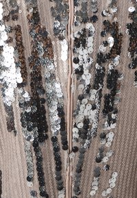 Tissu beige densément orné de rangées verticales de sequins noirs et argentés brillants créant un motif chatoyant.