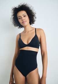 Svart bikini-sett med V-hals bralette og høytlivede bukser. Stoffet er glatt med minimale sømmer og en tettsittende silhuett.