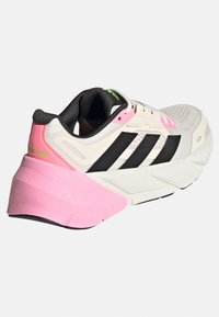 Sneaker de course blanche avec des rayures noires, un talon rose et des accents verts. Dessus texturé et semelle rembourrée pour le confort et le soutien.