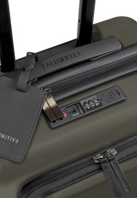 Hartschalenkoffer in Olivgrün mit doppeltem Reißverschluss, einem schwarzen ausziehbaren Griff, TSA-Schloss und einem abnehmbaren Gepäckanhänger.