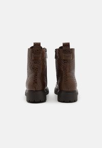 Bottes en cuir marron à la cheville avec un motif crocodile texturé, fermeture éclair à l'arrière et semelles épaisses, dotées d'une petite boucle au niveau du talon.