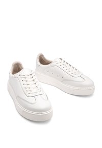 Białe skórzane trampki o teksturowanym wykończeniu, zaokrąglonym nosku i grubej, białej gumowej podeszwie. Posiadają płaskie sznurowadła oraz ozdobne perforacje.