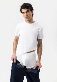 T-shirt en coton blanc à manches courtes, associé à un slip blanc et à un jean en denim foncé. Présente une texture lisse et une coupe décontractée.