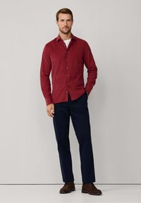 Bordeaux rood overhemd met een kraag, lange mouwen en een soepele textuur, gecombineerd met marineblauwe broek en bruine schoenen.