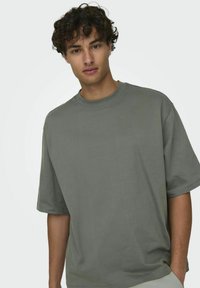 T-shirt à manches courtes surdimensionné en coton vert olive, doté d'un col rond et d'une coupe décontractée avec une texture lisse.