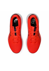 Baskets de sport rouge vif avec un dessus texturé, présentant des accents noirs et une semelle blanche. Les lacets sont plats et le design comprend des trous de ventilation.
