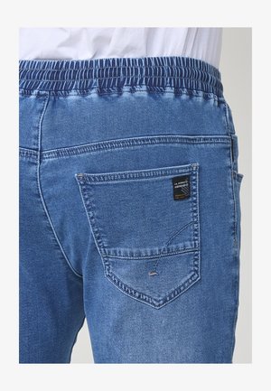 Jeans in denim con una cintura elastica blu scuro, lavaggio blu chiaro e una tasca posteriore con etichetta quadrata e dettagli cuciti.
