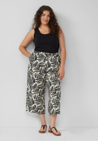 Zwarte tanktop gecombineerd met losse, cropped broek met een zwart en crèmekleurig bladerenpatroon. Sandalen maken de outfit compleet en benadrukken een casual uitstraling.