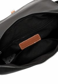 Schwarzes, mit Reißverschluss verschlossenes Täschchen, geöffnet, um ein Stoffinnenfutter mit einem braun gesteppten Lederetikett und einer inneren Reißverschlusstasche zu zeigen.