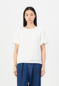 Hvit kortermet topp med en strukturert ribbet design. Rund hals, løs passform og mykt stoff. Kombinert med blå denimbukser.