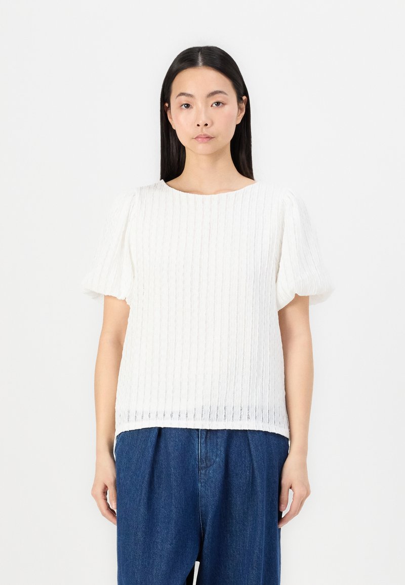 Hvit kortermet topp med en strukturert ribbet design. Rund hals, løs passform og mykt stoff. Kombinert med blå denimbukser.
