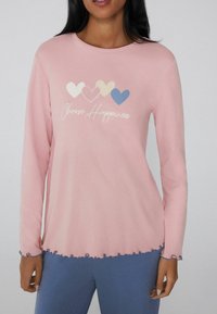 Blusa de manga larga rosa con un dobladillo en forma de ondas y acentos azules, que presenta un gráfico de tres corazones en colores pastel y el texto "Elige la felicidad."